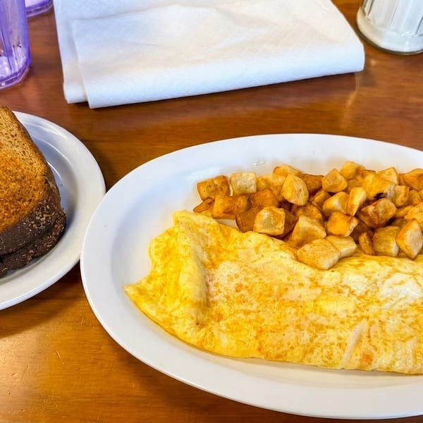 A breakfast plate with a golden omelet, crispy home fries, and dark rye toast on a wooden table.