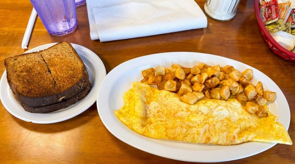 A breakfast plate with a golden omelet, crispy home fries, and dark rye toast on a wooden table.