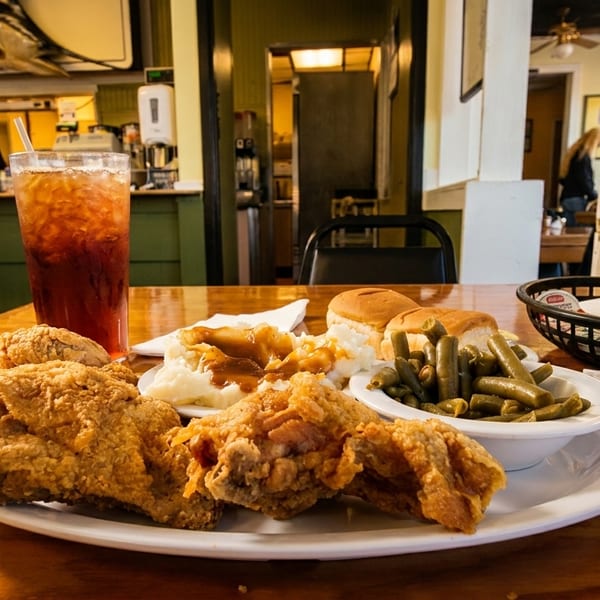 Fried chicken, mashed potatoes, green beans, and rolls on a wooden table in a diner.
