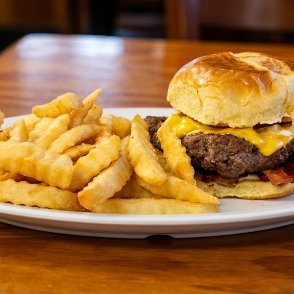 Cheeseburger with bacon and crinkle-cut fries on a white plate, on a wooden table.