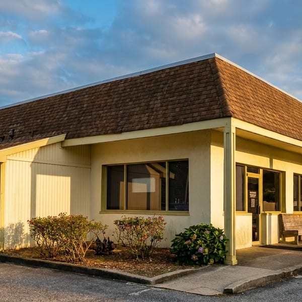 Exterior of a yellow building with a brown roof, large windows, and a covered porch.