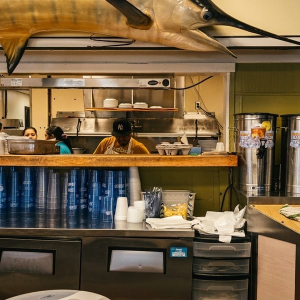 Restaurant kitchen with a mounted marlin, staff, and beverage dispensers.