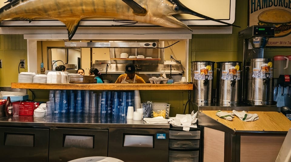 Restaurant kitchen with a mounted marlin, staff, and beverage dispensers.